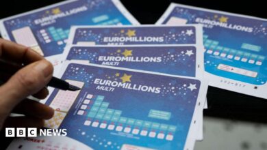 A hand holding a pen above five blue EuroMillions tickets.