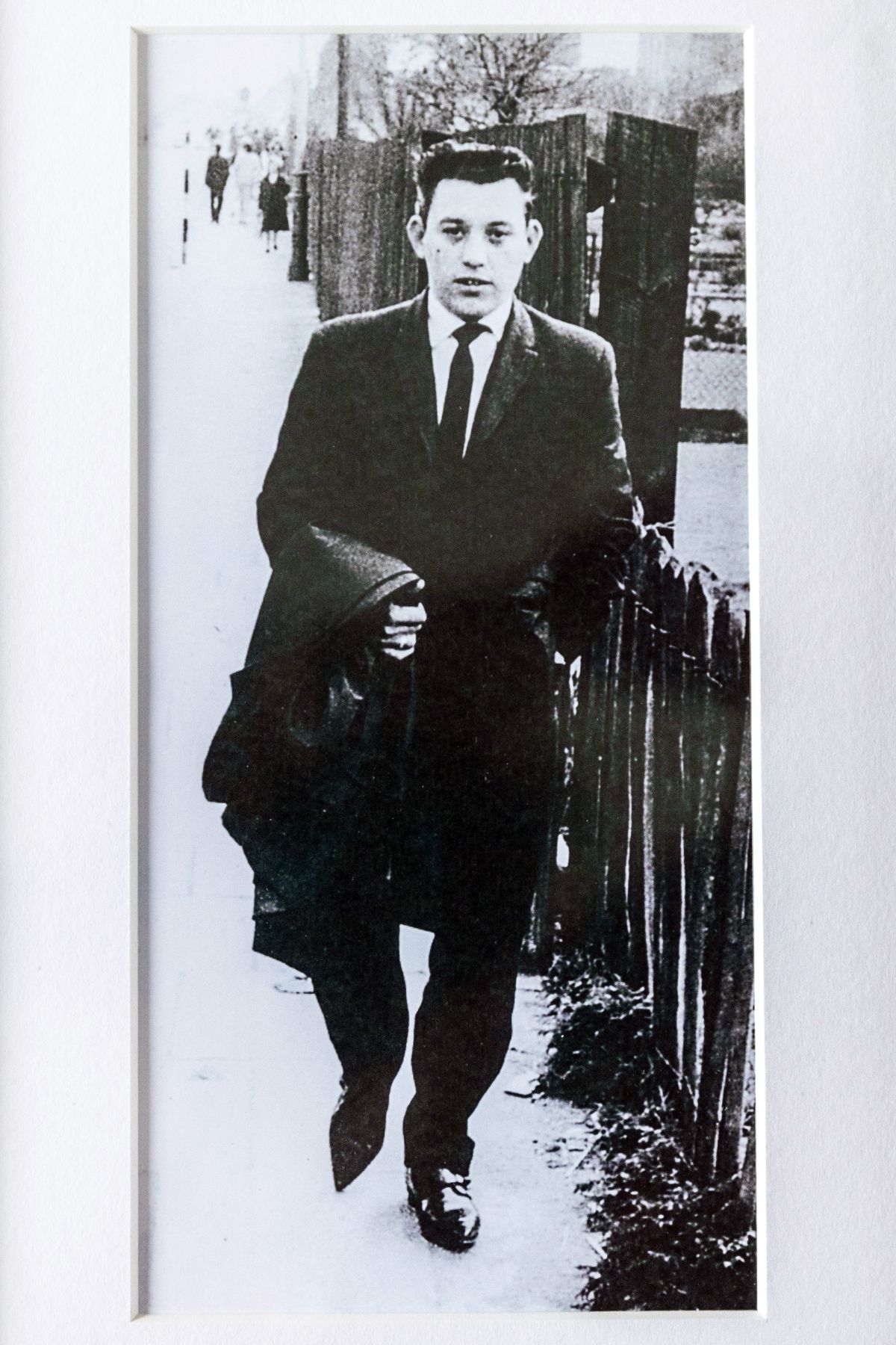 A black and white picture of David Whitby int he street wearing a suit and tie and carrying a coat