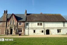 The image shows the Llanthony Secunda Priory building in bright sunshine. Two thirds of the building on the right is white walled and older looking, while the third on the left is made of red brick and more uniform.