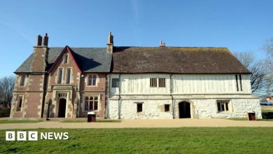 The image shows the Llanthony Secunda Priory building in bright sunshine. Two thirds of the building on the right is white walled and older looking, while the third on the left is made of red brick and more uniform.