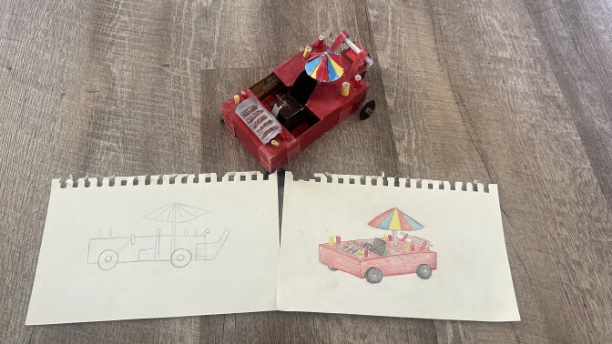 Two pieces of white notebook paper with a small model of a red soapbox sitting in front. The paper on the left has a basic pencil drawing of the car, while the paper on the right is a colored version.
