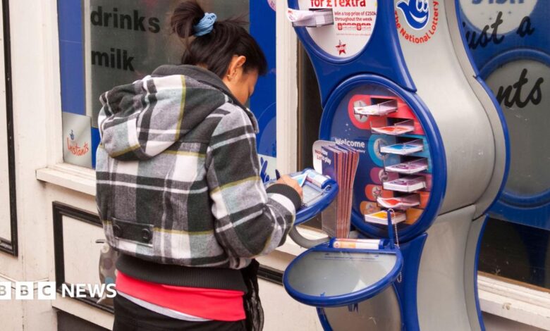 A woman fills out a form for a National Lottery ticket at a stand outside a shop