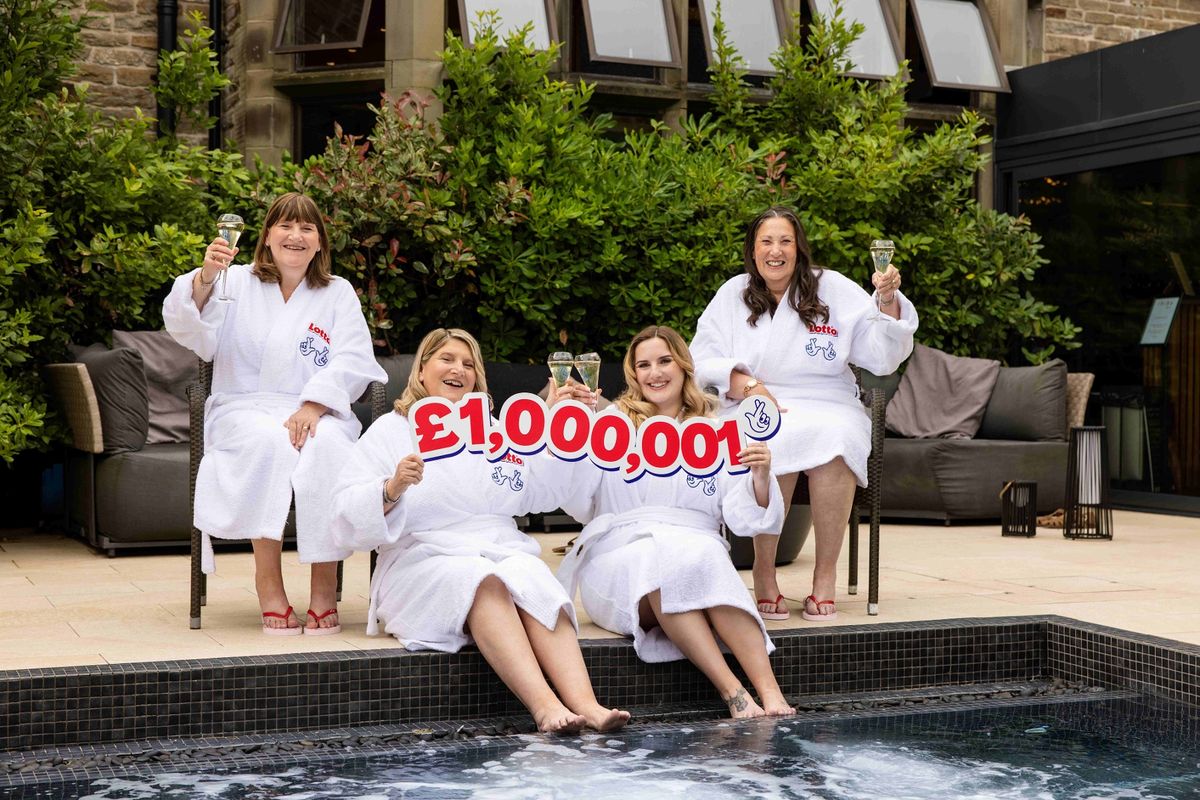 Four women at the side of a pool in dressing gowns, holding up a £1m sign