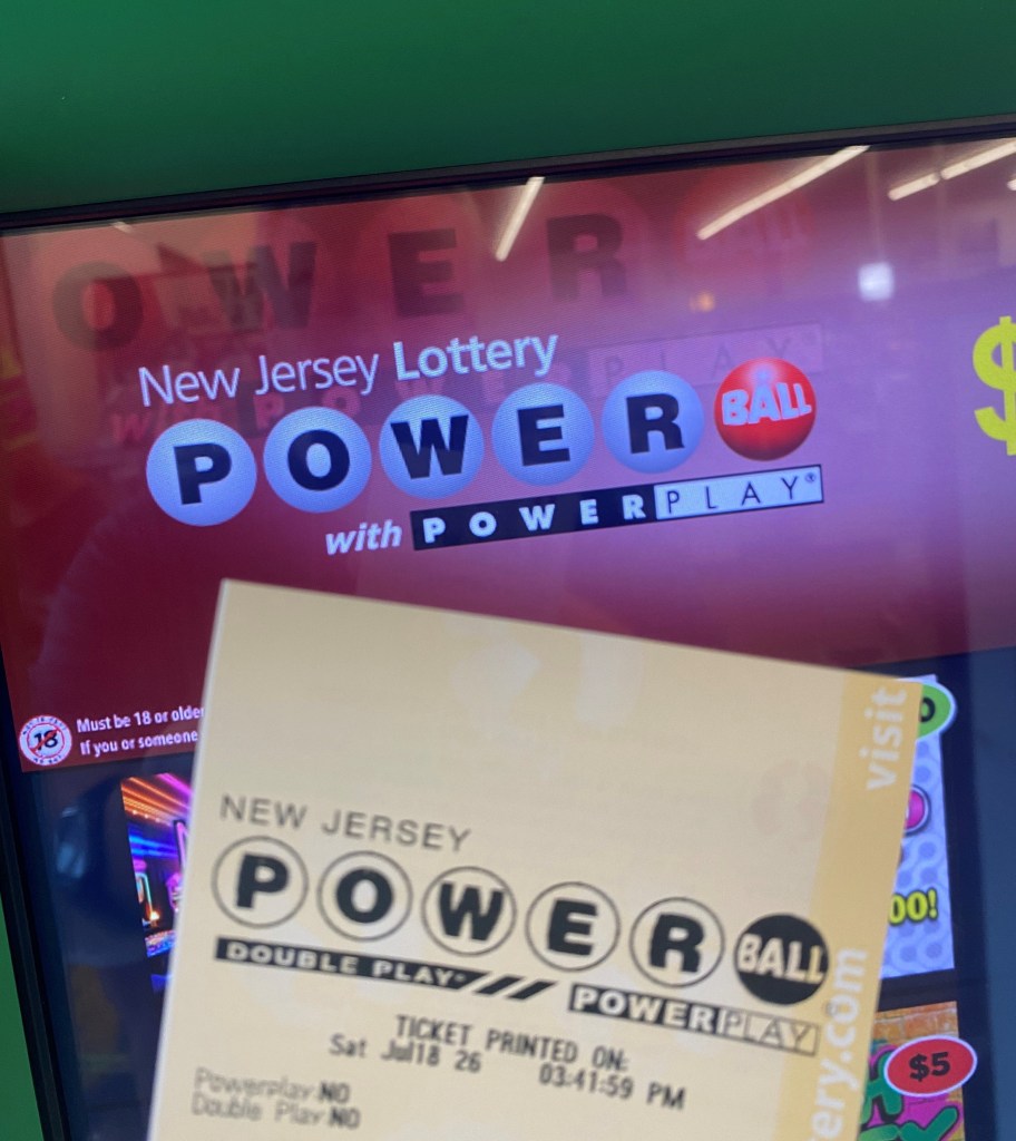 A Powerball lottery ticket in front of a digital screen showing the New Jersey Lottery Powerball logo.