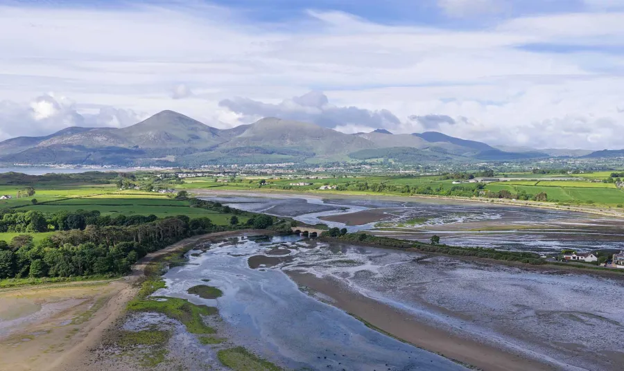 An aerial view of a landscape. There is an estuary in the foreground and tall hills on the horizon.