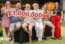 A family-of-six holding a cut out reading £1,000,000. The family consists of a mother and father, three adult daughters and an adult son. They are all smiling and holding glasses of champagne.