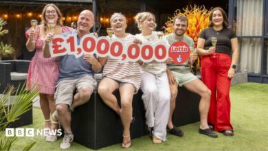 A family-of-six holding a cut out reading £1,000,000. The family consists of a mother and father, three adult daughters and an adult son. They are all smiling and holding glasses of champagne.
