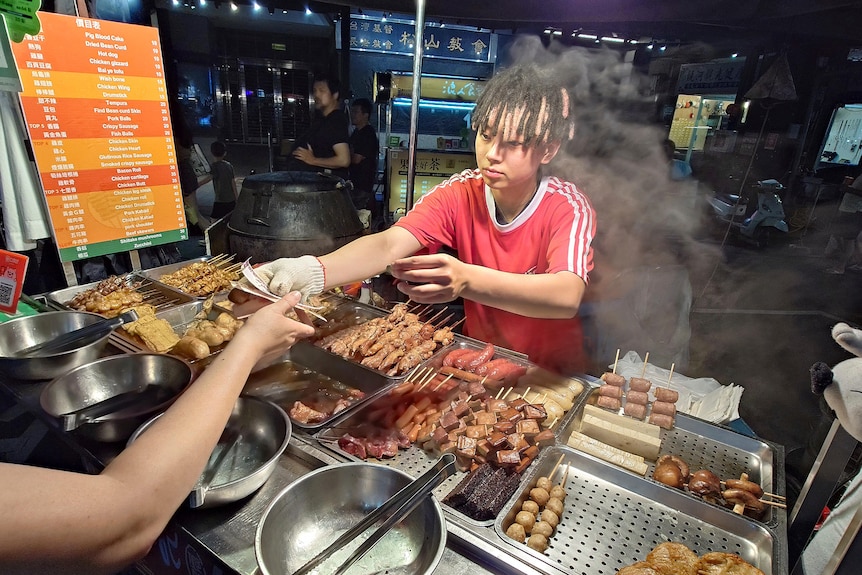 A man selling grilled meat skewers hands change to a customer.