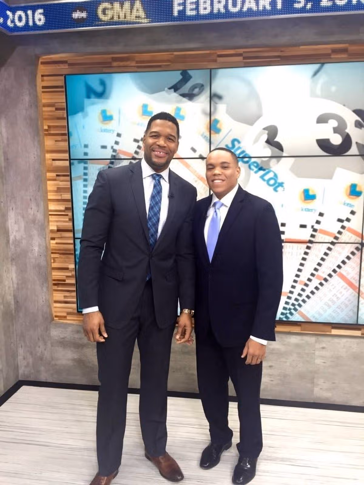 Two individuals dressed in formal attire are standing side by side in front of a large, visually engaging wall display. The background features a colorful, graphic design incorporating numbers and abstract shapes, suggesting an educational or informational context.